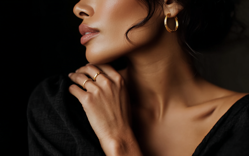 Close-up of a woman's face with gold earrings and rings on a dark background